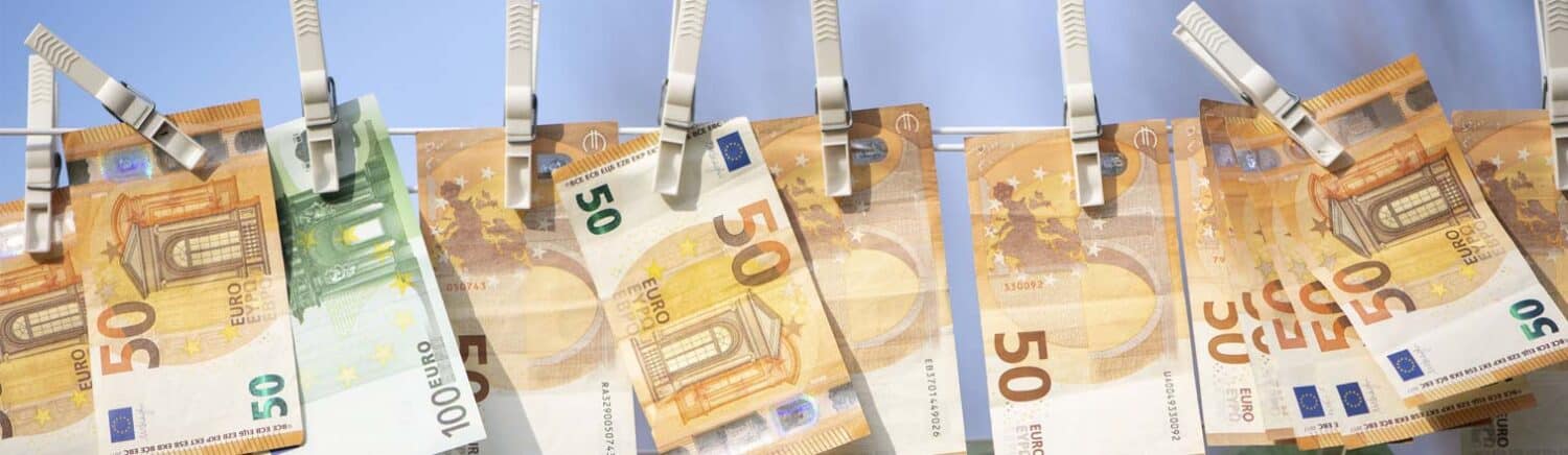 Mehrere Euro-Geldscheine hängen mit Wäscheklammern an einer Leine vor blauem Hintergrund.