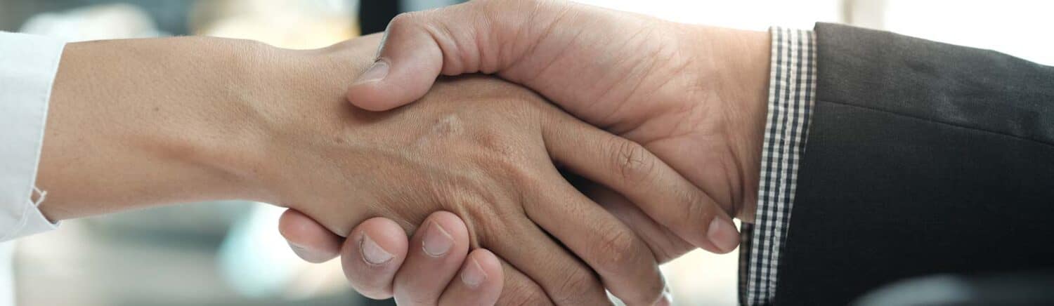 Zwei Personen geben sich die Hand, Nahaufnahme eines Händedrucks in geschäftlichem Kontext.