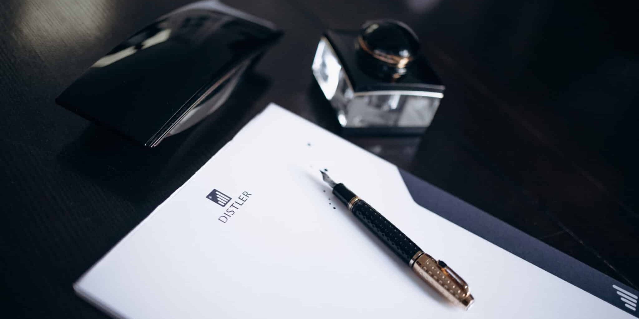 Eleganter Füllfederhalter auf gebrandetem Briefpapier neben Tintenfass und Lederaccessoire.
