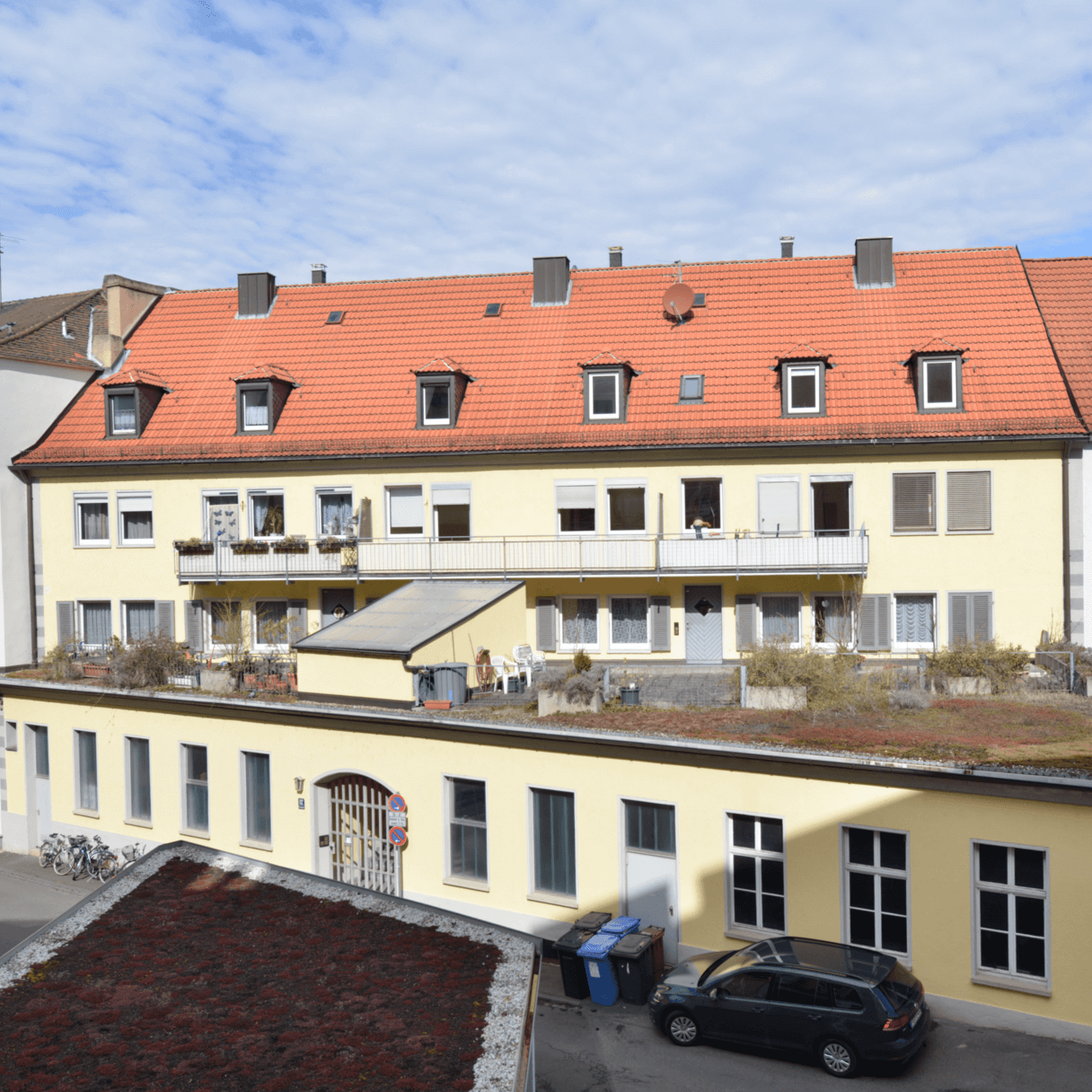Zweigeschossiges Wohngebäude mit heller Fassade und ausgebautem Dachgeschoss, Balkonreihe im Obergeschoss, Zufahrt mit Pflasterfläche im Vordergrund.
