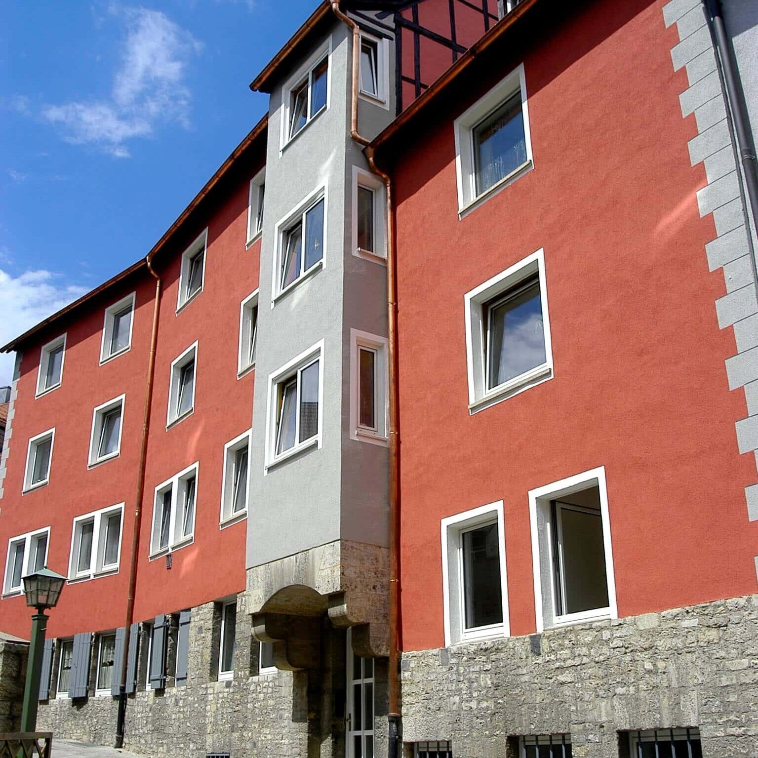 Dreigeschossiges Wohngebäude mit orangener Fassade und ausgebautem Dachgeschoss