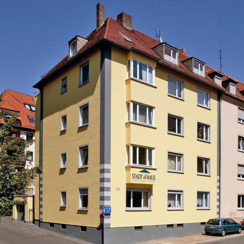 Viergeschossiges, gelbes Mehrfamilienhaus mit roten Dachziegeln und mehreren Dachgauben, Standort an der Franz-Ludwig-Straße in Würzburg.
