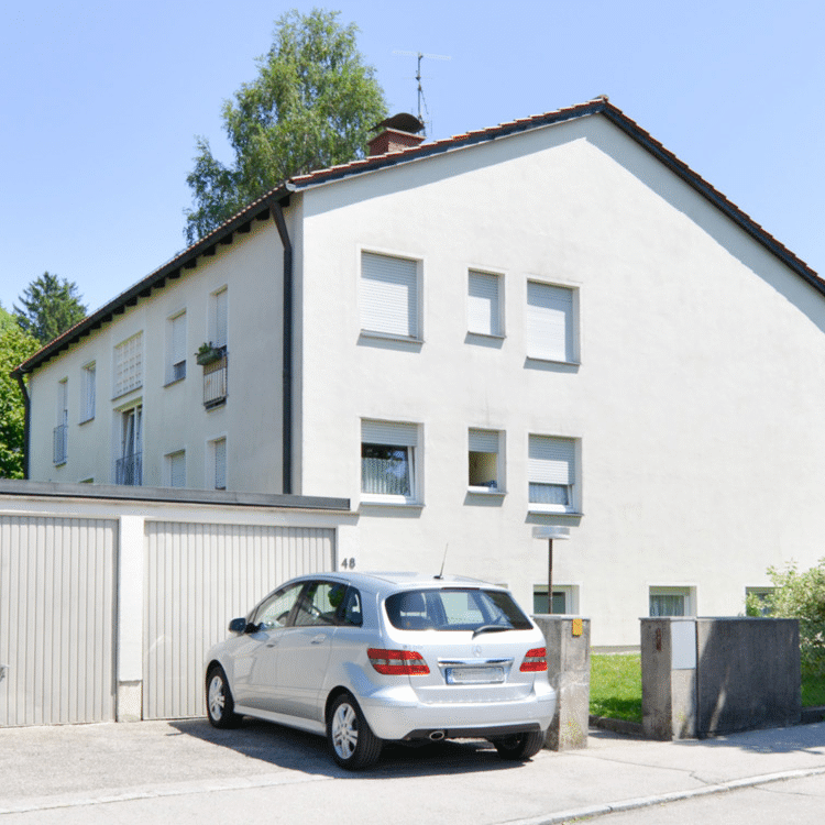 Zweigeschossiges weißes Wohngebäude mit Satteldach, rechteckigen Fenstern und angrenzender Garage, davor ein geparktes Auto; Standort Saalachstraße, Traunstein.