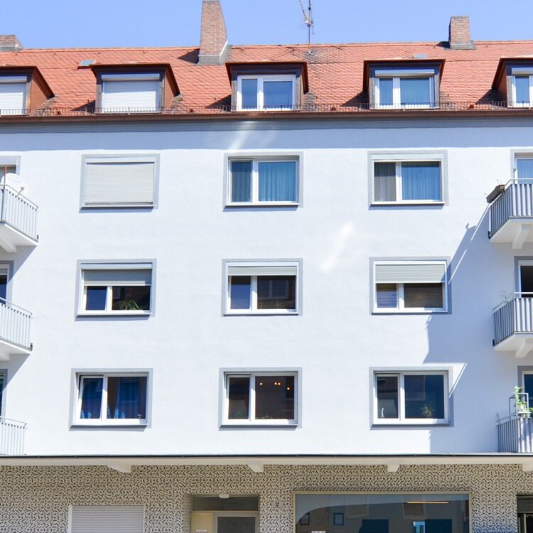 Viergeschossiges Gebäude mit weißer Fassade, mehreren Fenstern, einem Ladengeschäft im Erdgeschoss und Balkonen zur Straße.